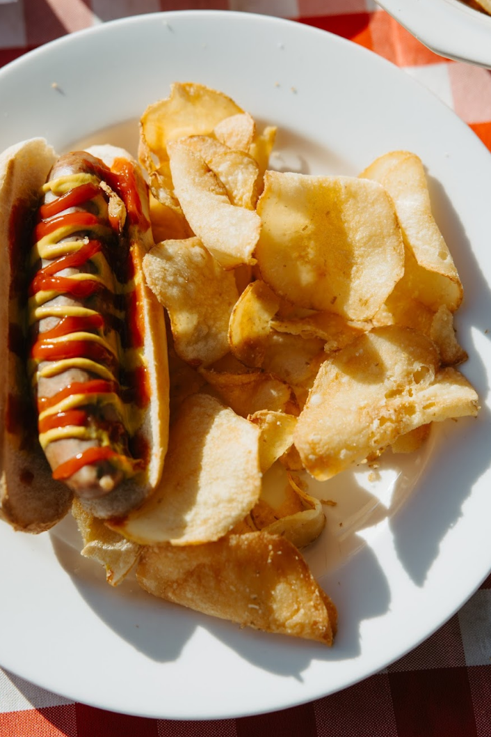Various snacks displayed on a white plate on top of a picnic table including kettle chips from Rosie's Chips.