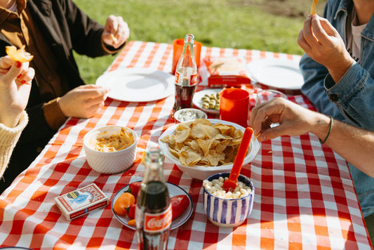 People eating snacks on a picnic table including the best tallow chips from Rosie's Chips while staying outdoors.