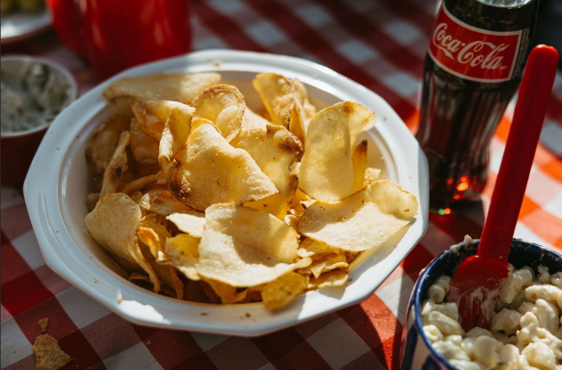 Small batch potato chips on a picnic table with other snacks and drinks.