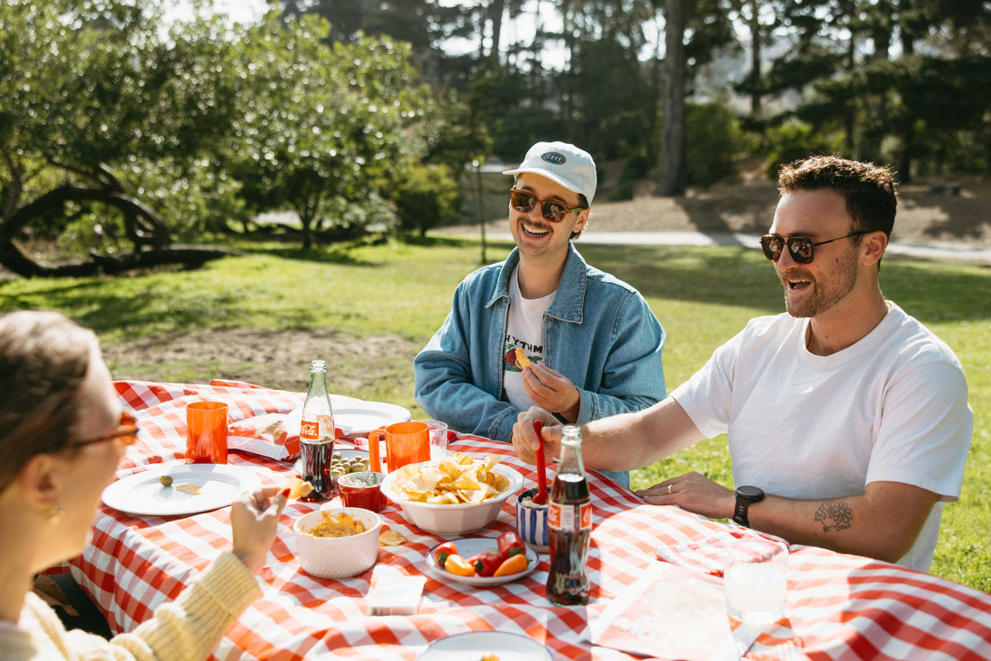 Men eating tallow potato chips together on a table with two friends and grassy background.