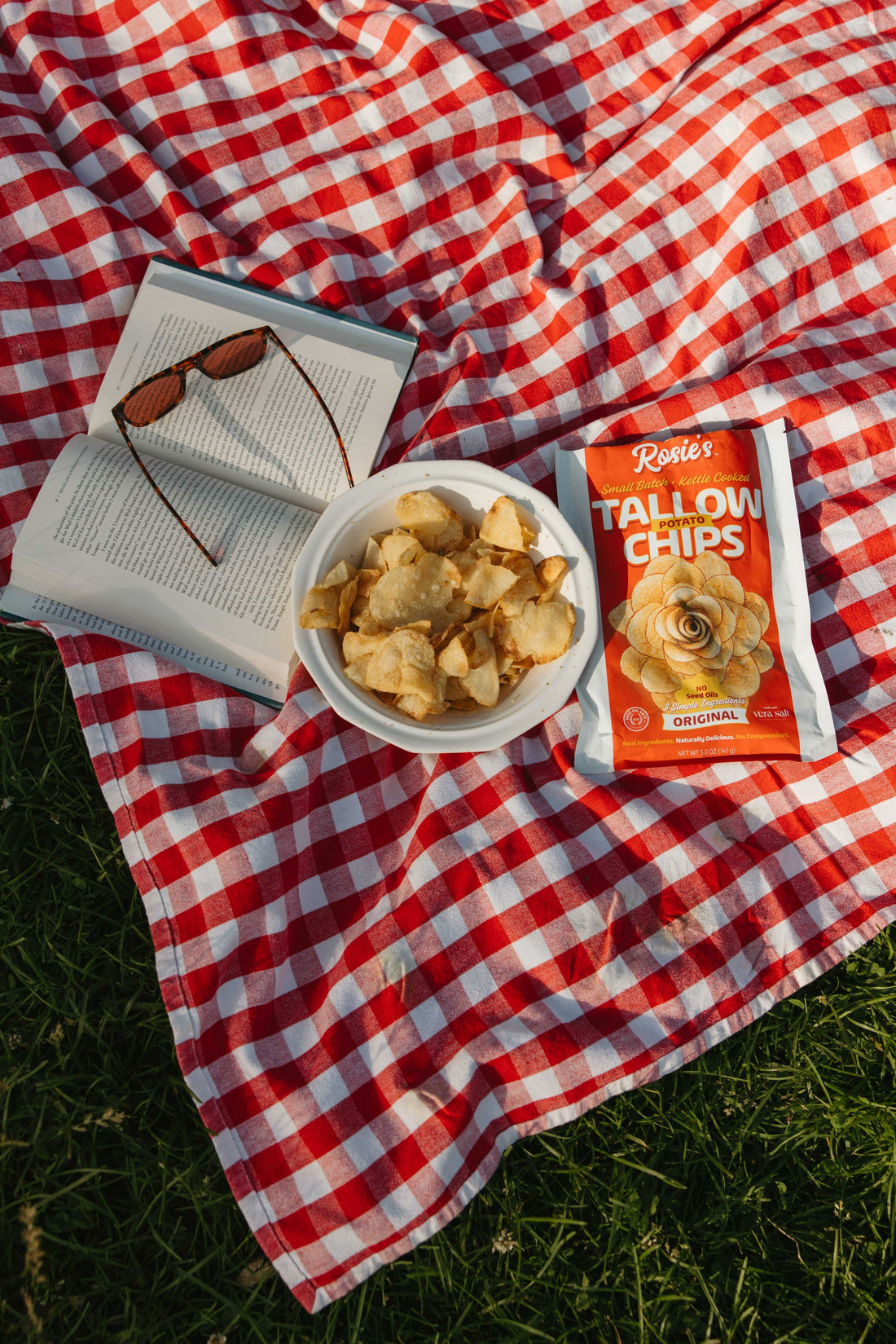 Seed oil free chips shown on a bowl with a book with a sunglass on it on a picnic mat.